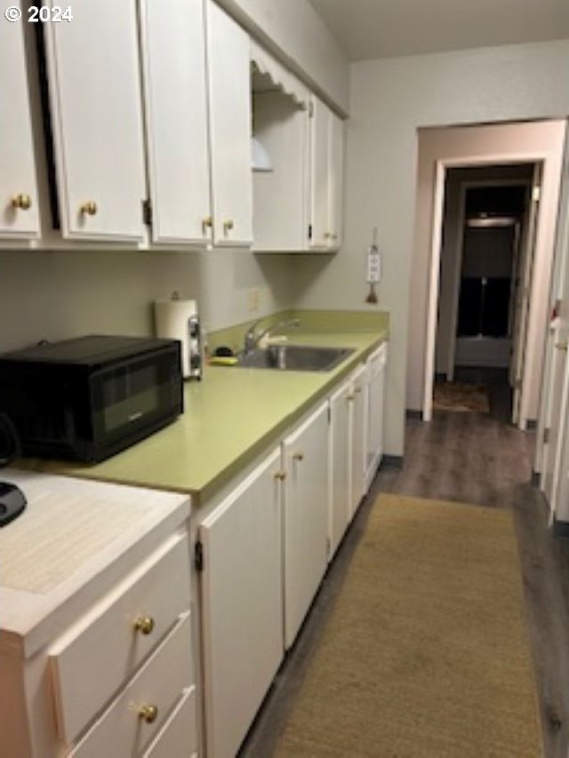 kitchen with wood finished floors, white cabinets, a sink, and light countertops