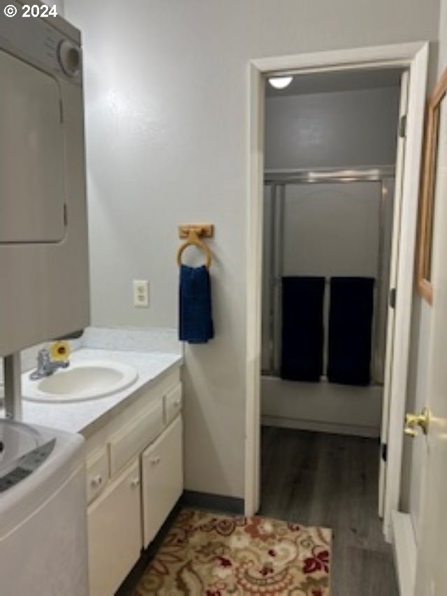 bathroom with a shower with door, vanity, wood-type flooring, and stacked washer / drying machine