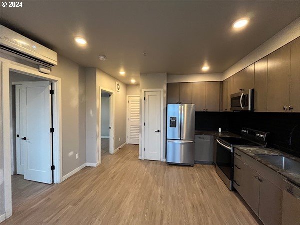 kitchen with sink, light hardwood / wood-style flooring, dark stone countertops, appliances with stainless steel finishes, and a wall unit AC