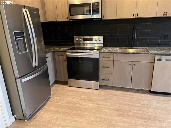 kitchen with light wood-type flooring, stainless steel appliances, backsplash, and sink