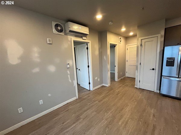 interior space with an AC wall unit, stainless steel fridge with ice dispenser, and hardwood / wood-style floors