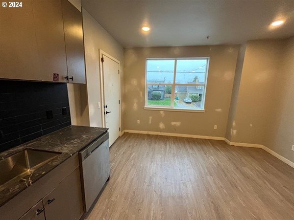 kitchen featuring light wood-type flooring, backsplash, sink, dark stone countertops, and dishwasher