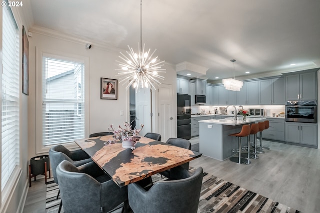 dining area featuring ornamental molding, light hardwood / wood-style flooring, a notable chandelier, and sink