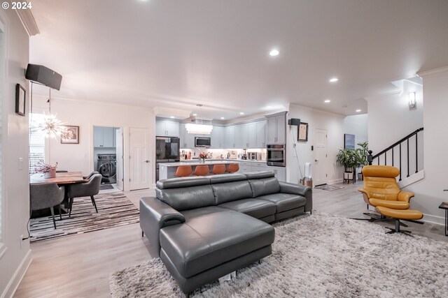 living room featuring washer / dryer, ornamental molding, and light hardwood / wood-style flooring