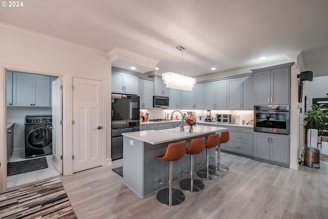 kitchen with a kitchen bar, light wood-type flooring, stainless steel appliances, and hanging light fixtures