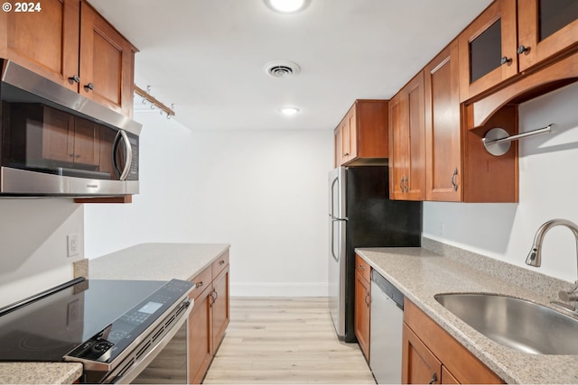 kitchen featuring light stone countertops, stainless steel appliances, light hardwood / wood-style floors, and sink