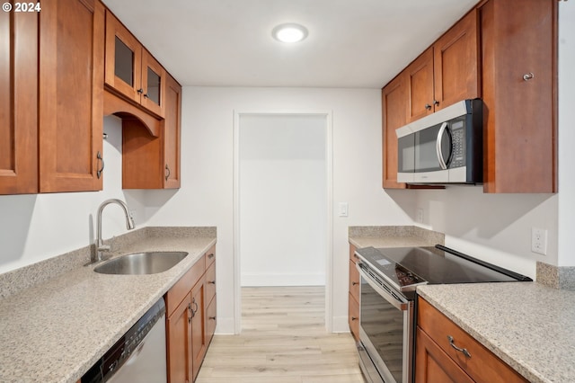 kitchen with light hardwood / wood-style floors, light stone countertops, sink, and appliances with stainless steel finishes