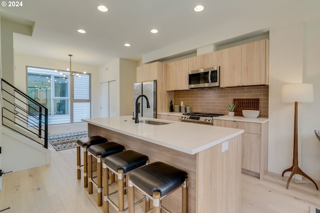 kitchen with a kitchen island with sink, pendant lighting, appliances with stainless steel finishes, and light hardwood / wood-style flooring