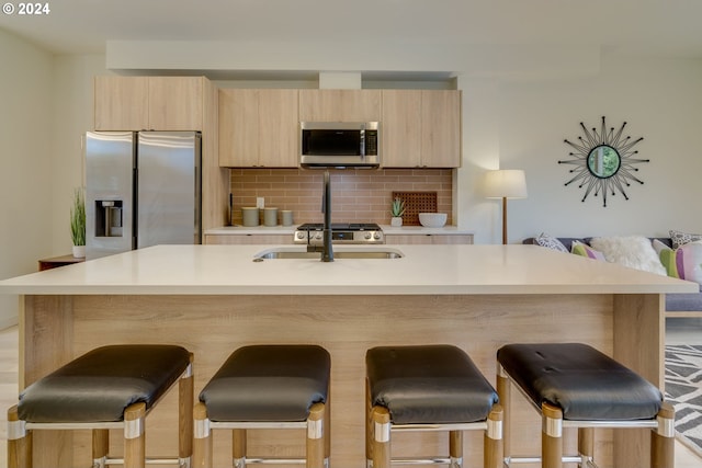 kitchen with appliances with stainless steel finishes, backsplash, a kitchen island with sink, and a breakfast bar area