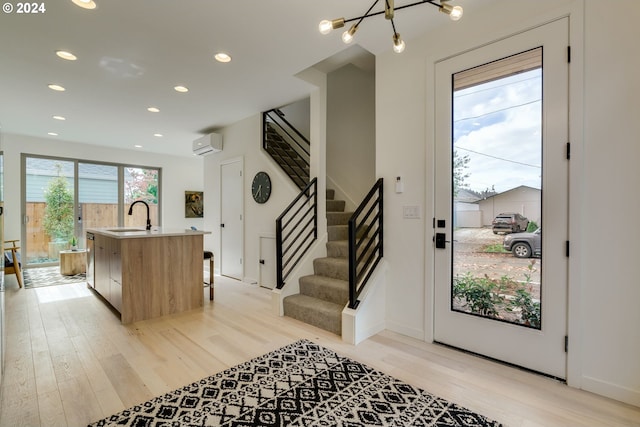 foyer entrance with a wall mounted air conditioner, sink, light hardwood / wood-style floors, and a chandelier