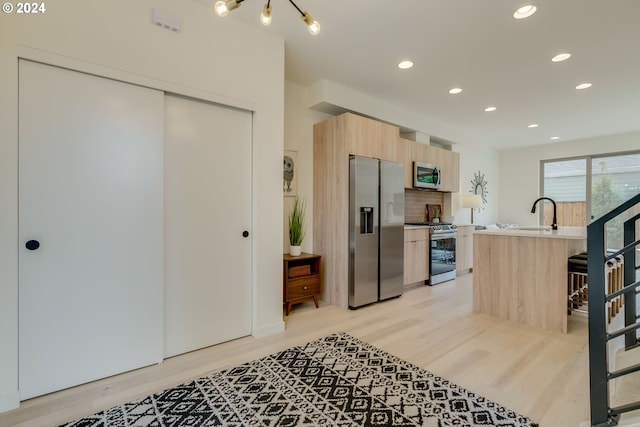 kitchen featuring light brown cabinets, a kitchen bar, light hardwood / wood-style floors, stainless steel appliances, and a kitchen island with sink