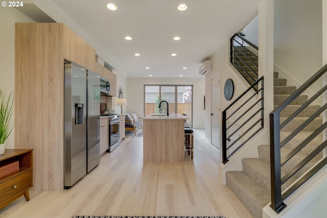 kitchen with a wall unit AC, light wood-type flooring, a breakfast bar area, stainless steel appliances, and an island with sink