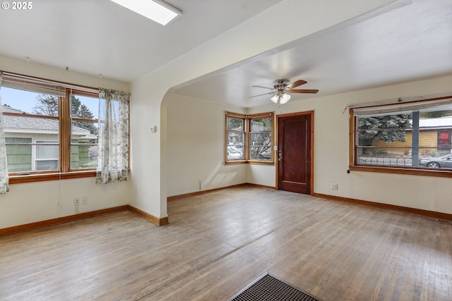 spare room featuring baseboards, arched walkways, a healthy amount of sunlight, and wood finished floors