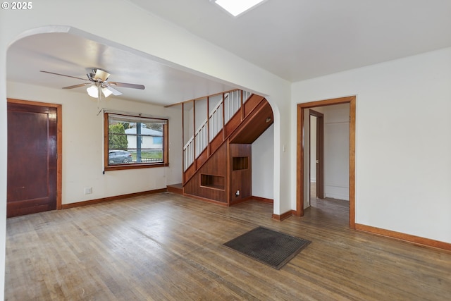 empty room featuring arched walkways, stairs, baseboards, and wood finished floors