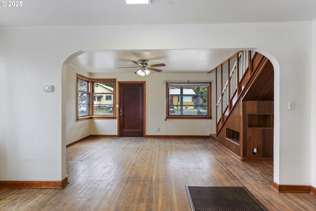 unfurnished living room featuring stairs, wood finished floors, arched walkways, and baseboards