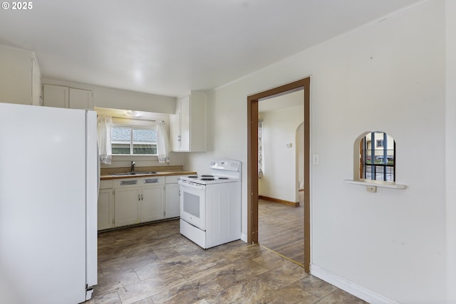 kitchen featuring baseboards, arched walkways, white appliances, white cabinetry, and a sink