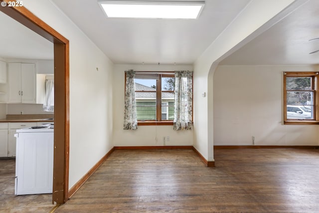 empty room featuring baseboards, arched walkways, and wood finished floors