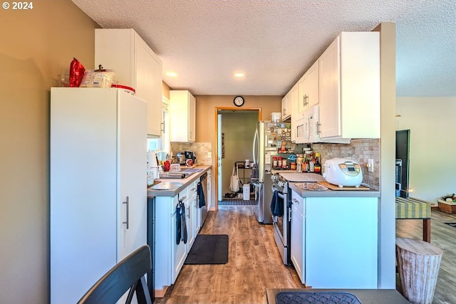 kitchen featuring wood-type flooring, backsplash, white appliances, and white cabinetry