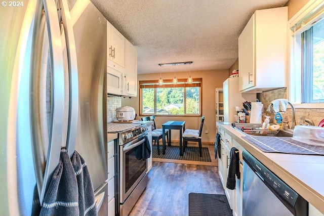 kitchen with pendant lighting, stainless steel appliances, dark hardwood / wood-style flooring, and white cabinetry