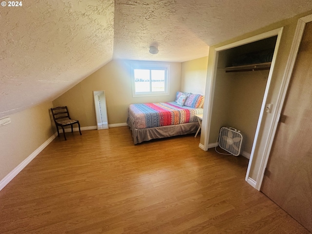 bedroom featuring a textured ceiling, a closet, lofted ceiling, and hardwood / wood-style floors