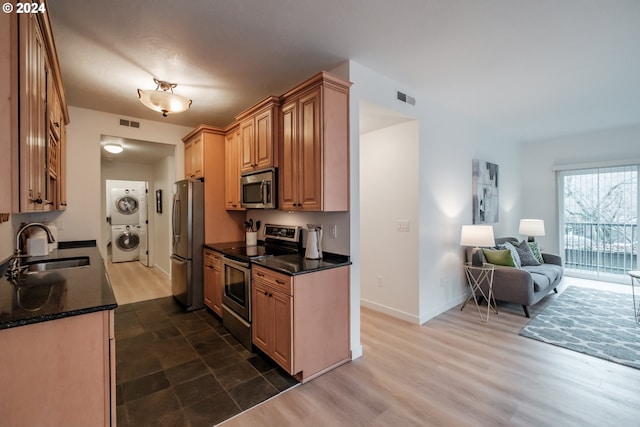 kitchen with sink, dark hardwood / wood-style floors, dark stone countertops, stacked washing maching and dryer, and appliances with stainless steel finishes