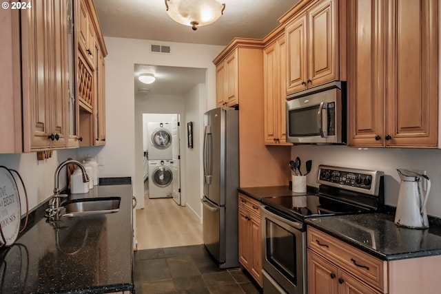 kitchen featuring appliances with stainless steel finishes, stacked washer / dryer, dark stone counters, and sink