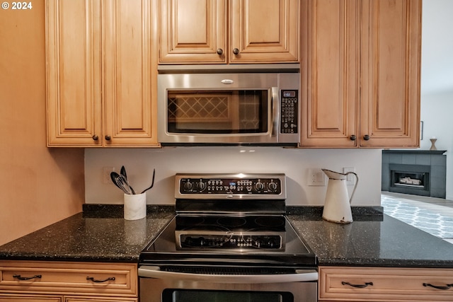 kitchen featuring dark stone counters, a tiled fireplace, and stainless steel appliances