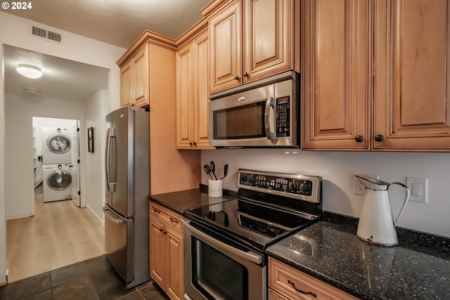 kitchen featuring dark hardwood / wood-style floors, dark stone countertops, stacked washer and dryer, and appliances with stainless steel finishes