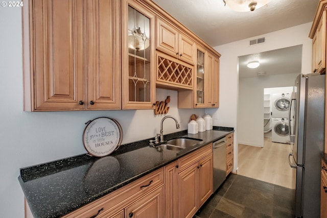 kitchen with sink, dark stone counters, stacked washer and clothes dryer, and appliances with stainless steel finishes