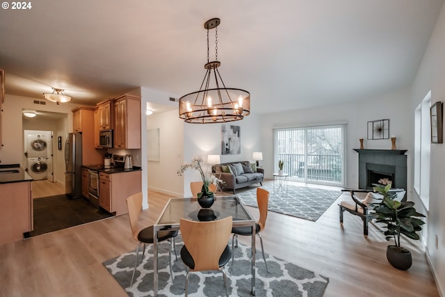 dining room with dark hardwood / wood-style flooring, stacked washer and dryer, a tile fireplace, and an inviting chandelier