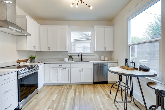 kitchen featuring stainless steel appliances, wall chimney range hood, sink, and white cabinets