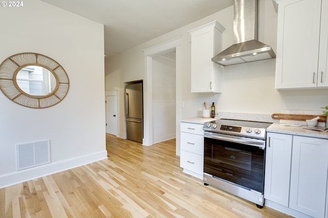 kitchen with appliances with stainless steel finishes, white cabinetry, wall chimney range hood, and light wood-type flooring