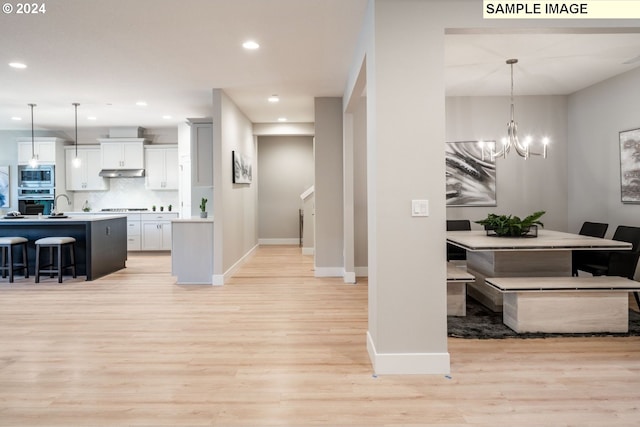 kitchen featuring stainless steel appliances, a chandelier, decorative light fixtures, a kitchen island with sink, and white cabinets