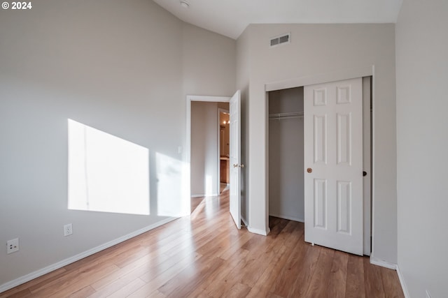 unfurnished bedroom with light hardwood / wood-style floors, high vaulted ceiling, and a closet