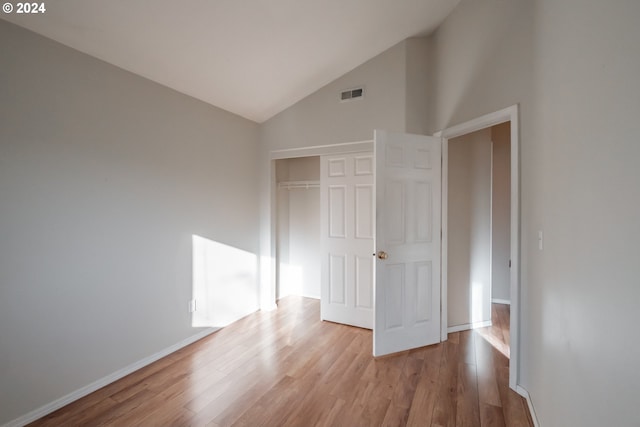 unfurnished bedroom featuring high vaulted ceiling, light wood-type flooring, and a closet