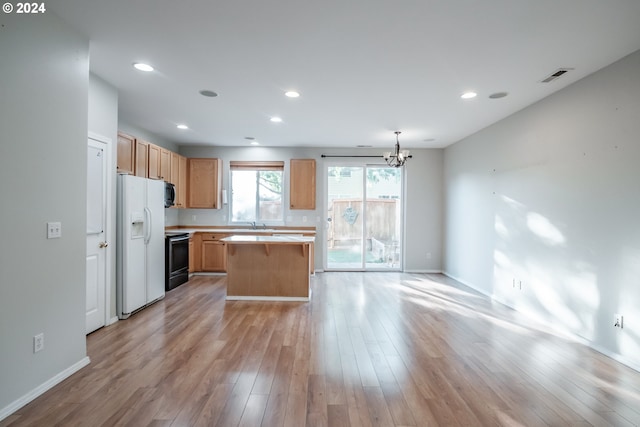 kitchen with light wood-type flooring, white refrigerator with ice dispenser, hanging light fixtures, a kitchen island, and black stove