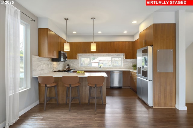 kitchen featuring stainless steel appliances, decorative light fixtures, kitchen peninsula, a wealth of natural light, and dark hardwood / wood-style flooring