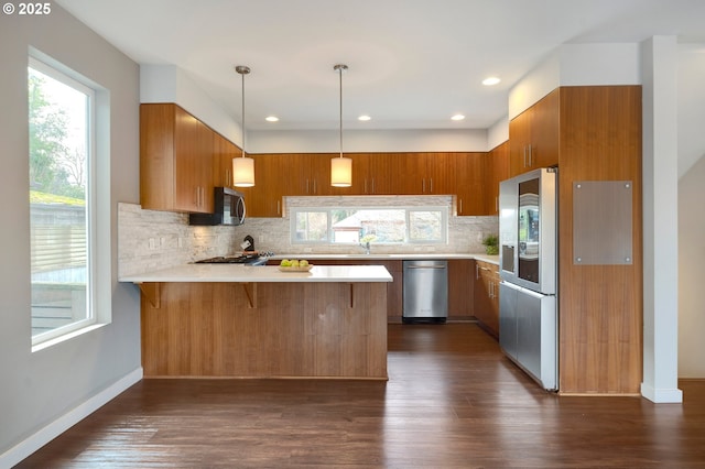 kitchen with stainless steel appliances, kitchen peninsula, backsplash, dark hardwood / wood-style flooring, and pendant lighting