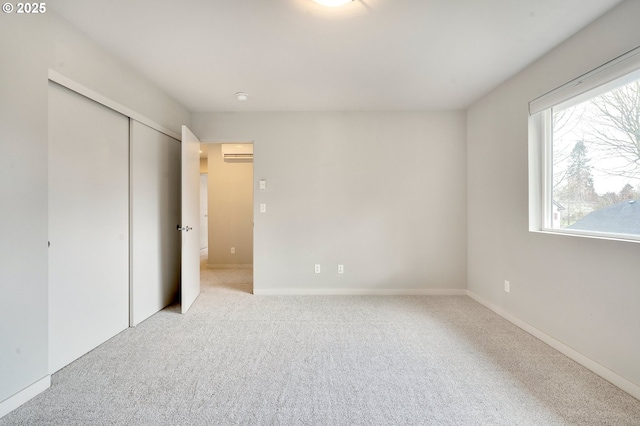 unfurnished bedroom with an AC wall unit, light colored carpet, a closet, and multiple windows