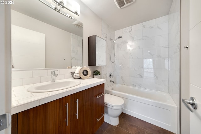 full bathroom with toilet, tile patterned flooring, decorative backsplash, tiled shower / bath combo, and vanity