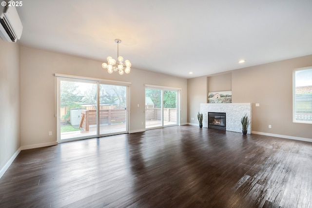 unfurnished living room with dark wood-type flooring, a stone fireplace, an inviting chandelier, and an AC wall unit