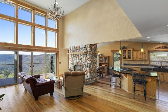 living room with an inviting chandelier, high vaulted ceiling, light hardwood / wood-style flooring, and a fireplace