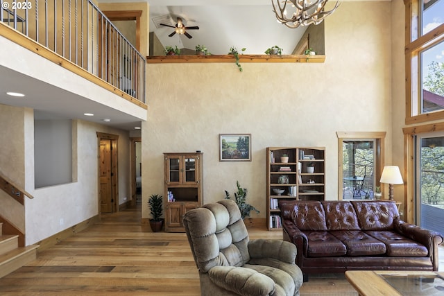 living room featuring light hardwood / wood-style flooring, ceiling fan with notable chandelier, and a towering ceiling