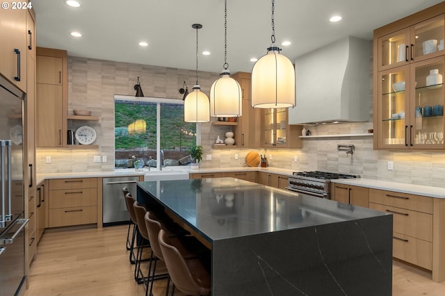 kitchen featuring pendant lighting, a kitchen island, wall chimney range hood, stainless steel appliances, and light wood-type flooring