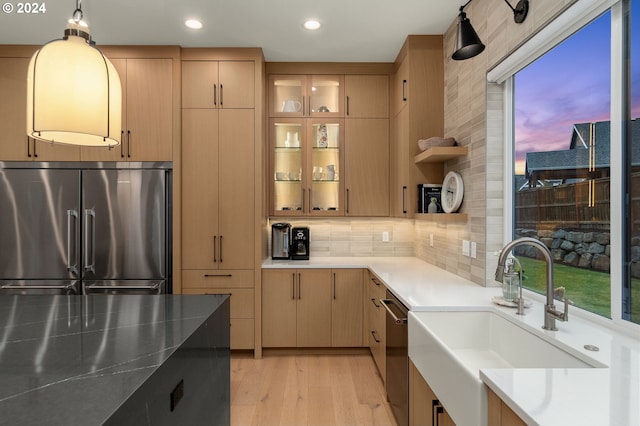 kitchen with light wood-type flooring, light brown cabinets, sink, stainless steel appliances, and hanging light fixtures