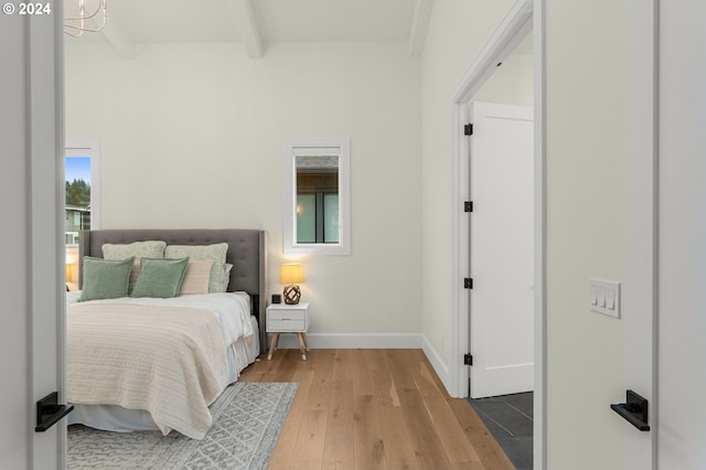 bedroom featuring beamed ceiling, multiple windows, and light hardwood / wood-style floors