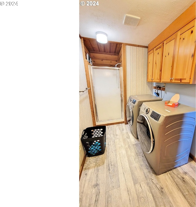 washroom with a textured ceiling, light wood-type flooring, cabinet space, washing machine and dryer, and visible vents