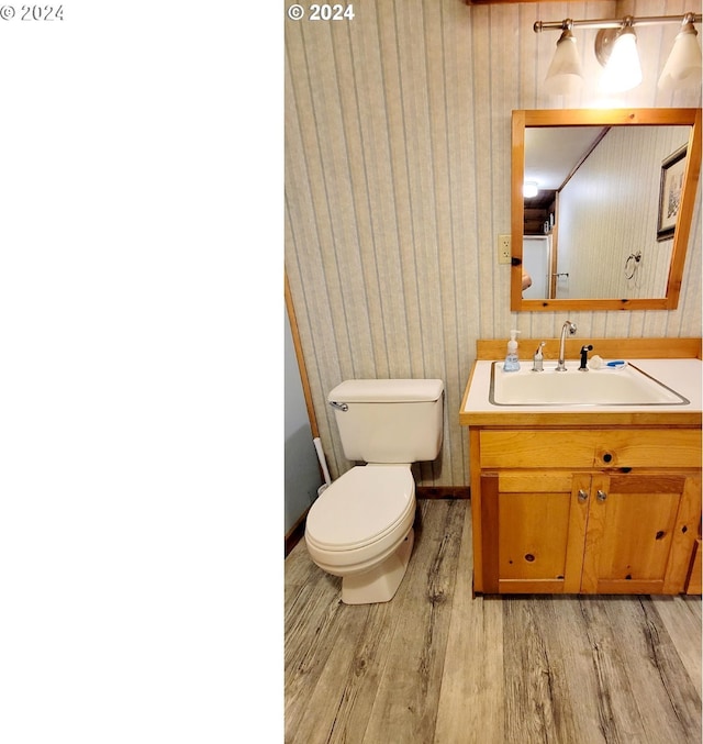half bathroom with baseboards, wood finished floors, vanity, and toilet