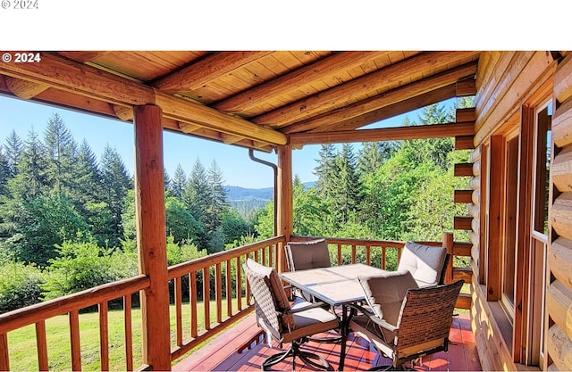 wooden terrace featuring a yard, outdoor dining space, a forest view, and a mountain view