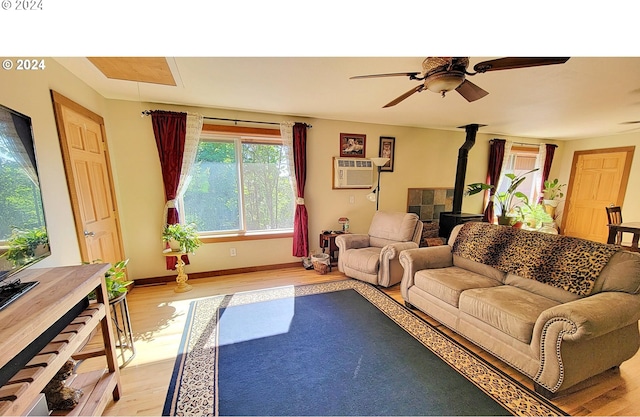 living room with a wall mounted AC, a wood stove, ceiling fan, and light hardwood / wood-style flooring